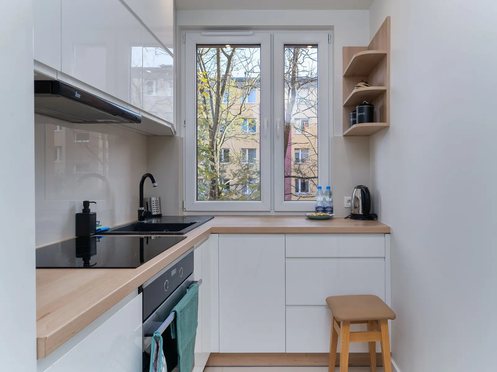 Petite cuisine en longueur d'appartement, meubles clairs et fenêtre au fond