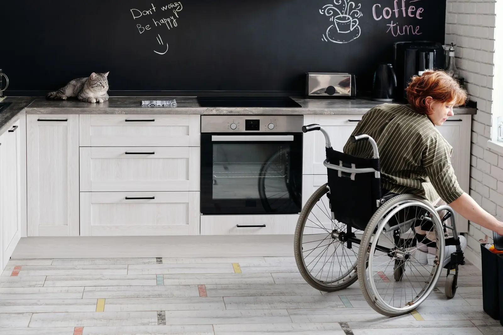 Personne en fauteuil roulant à son plan de travail, dans une cuisine aux meubles blancs