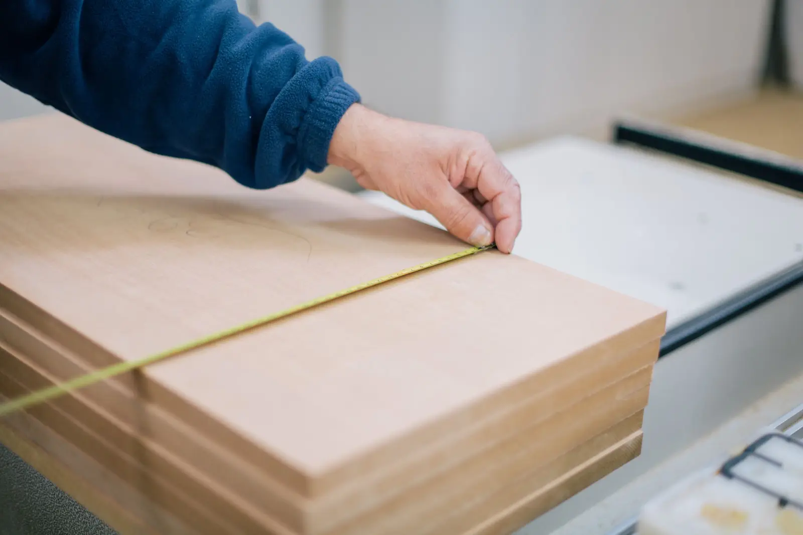 Mesure au ruban d'un panneau avant découpe, en atelier