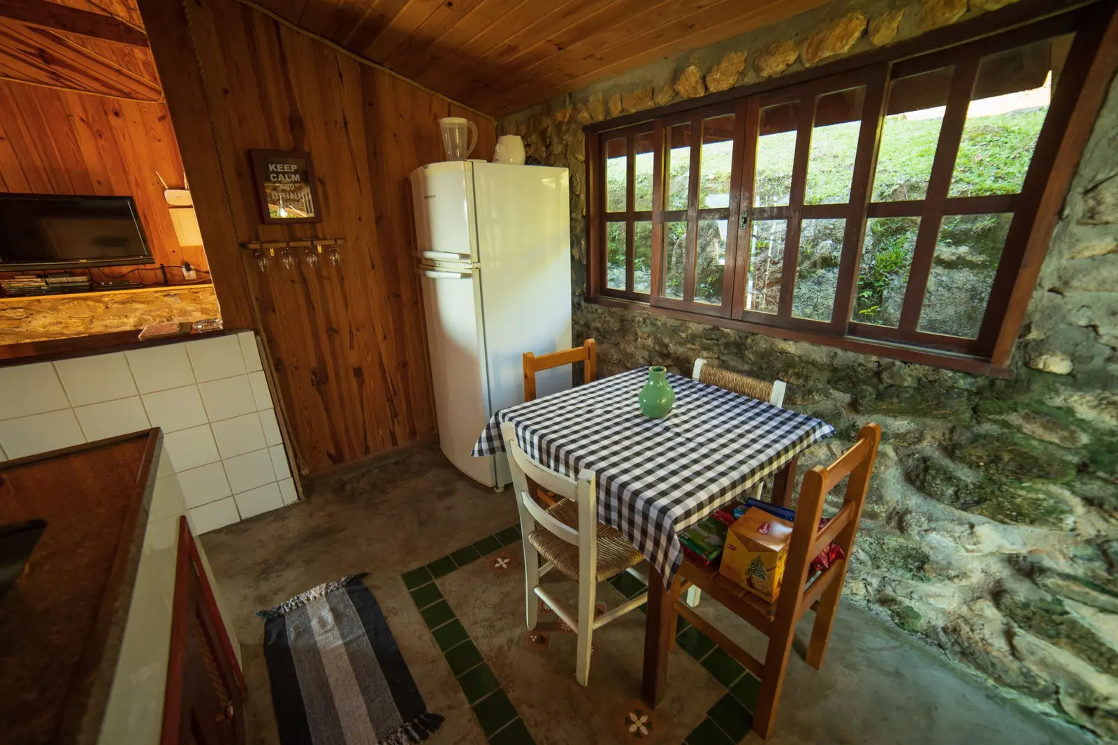 Cuisine rustique aux murs de pierre, table à nappe à carreaux et plafond en bois